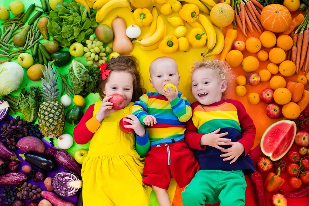 young children lying down amidst a rainbow of colourful fruits and vegetables
