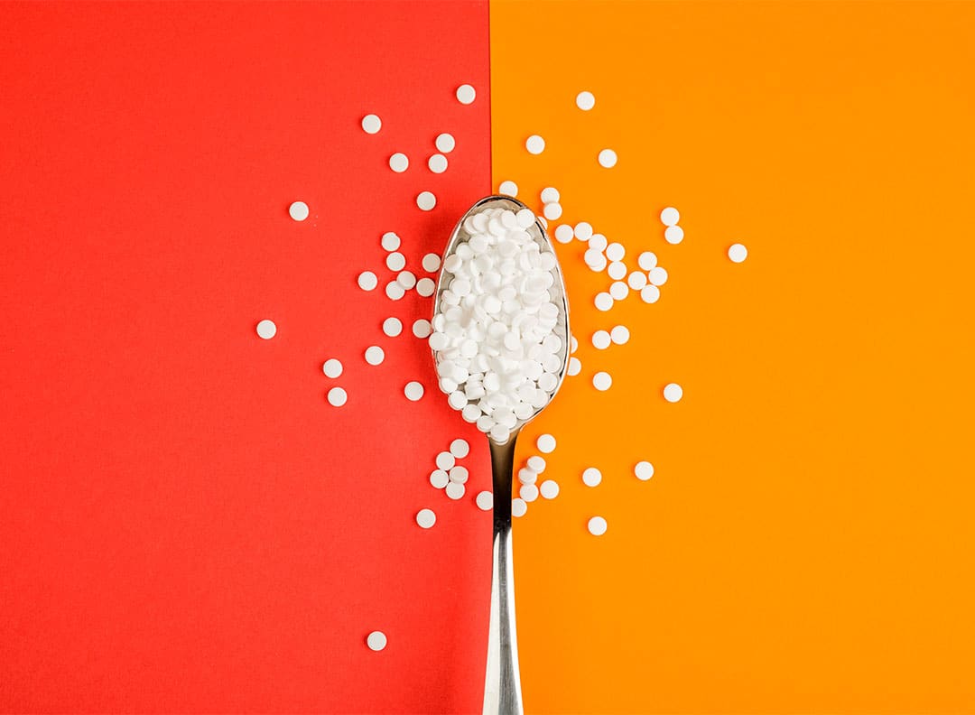 tiny white artificial sugar tablets on a spoon against an orange-red background
