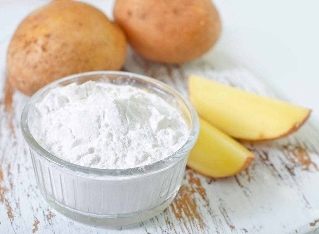 white powder potato starch, a natural thickener, in a small glass bowl on a table with potatoes