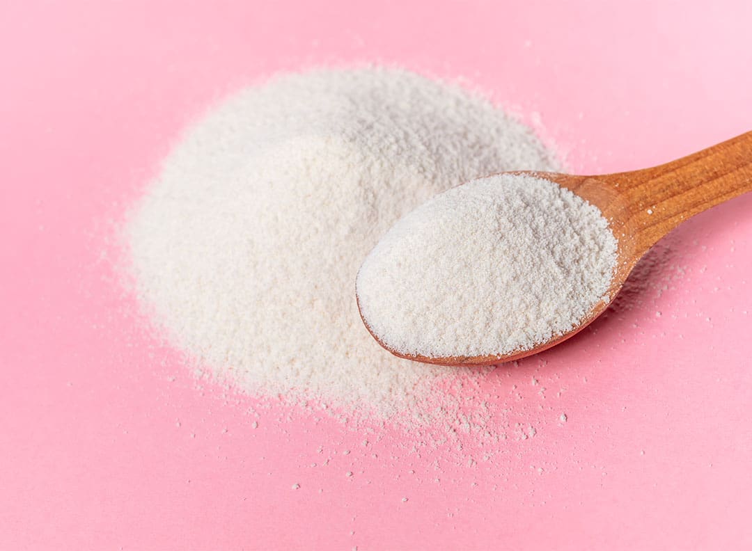 white powdered xylitol, a natural sweetener, on a wooden spoon and piled on a pink surface