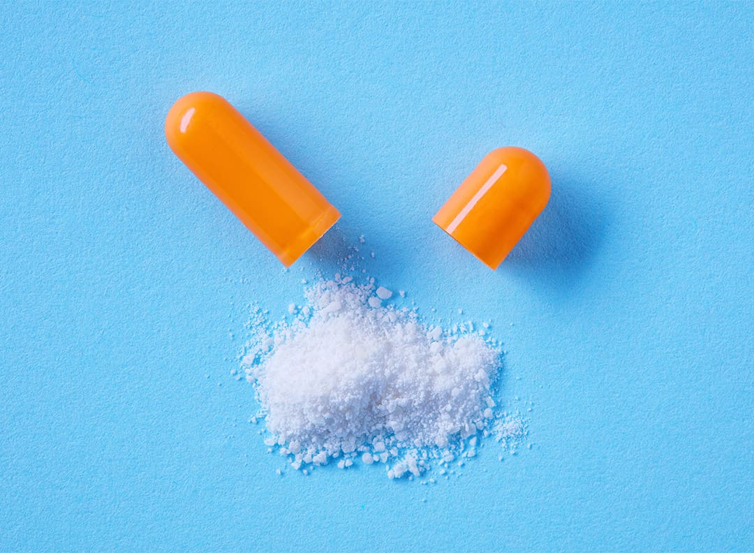 white powder spilling out of opened orange capsule, against a blue background