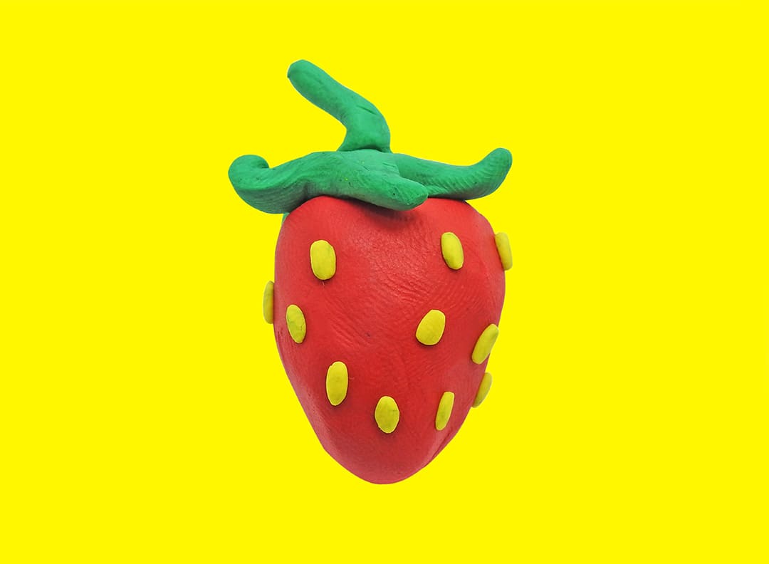 artificial strawberry made of clay against a yellow background