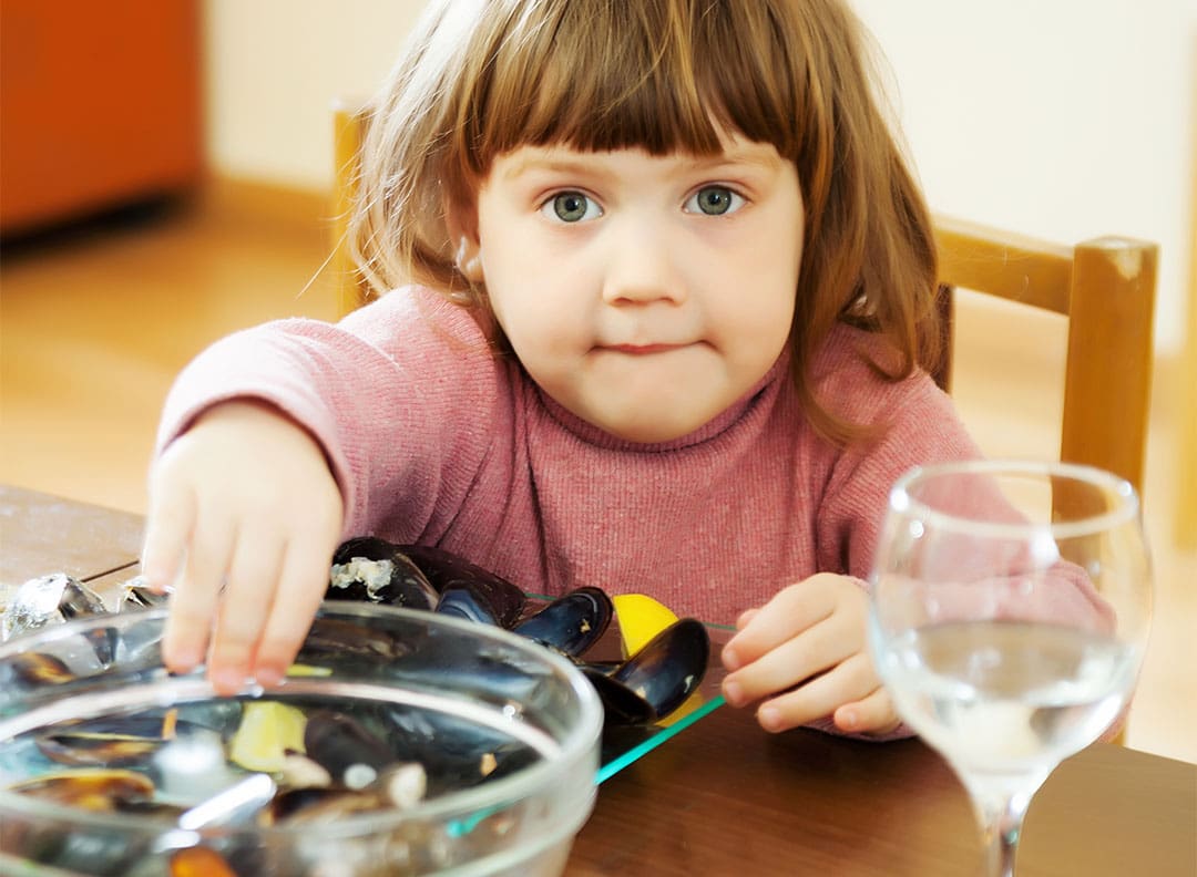 young girl eating mussels at a kitchen table