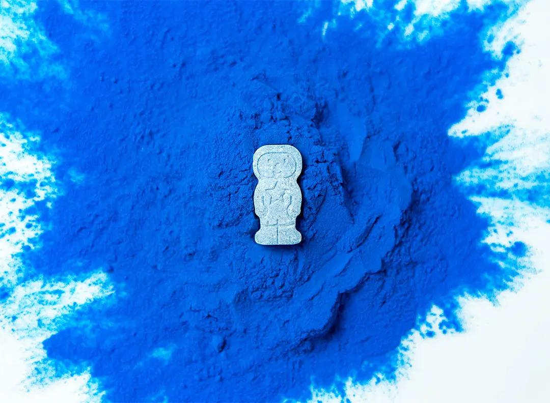 a nutrient-dense, vibrant blue powder, which is derived from algae, spilled onto a white table, with a StarMulti tablet on top