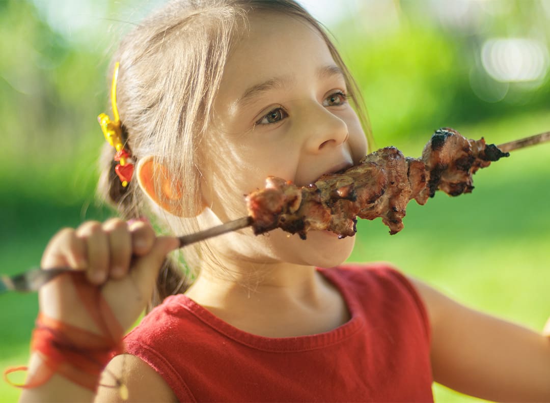 girl in a red shirt eating cooked meat on a skewer