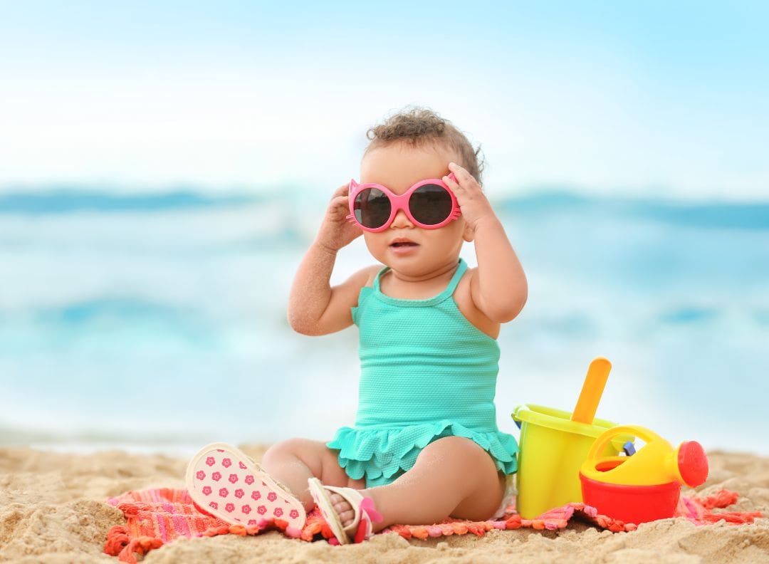 girl toddler wearing sunglasses sitting on the sand at the beach