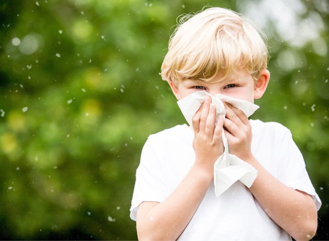 boy blowing his nose while surrounded by pollen in the air