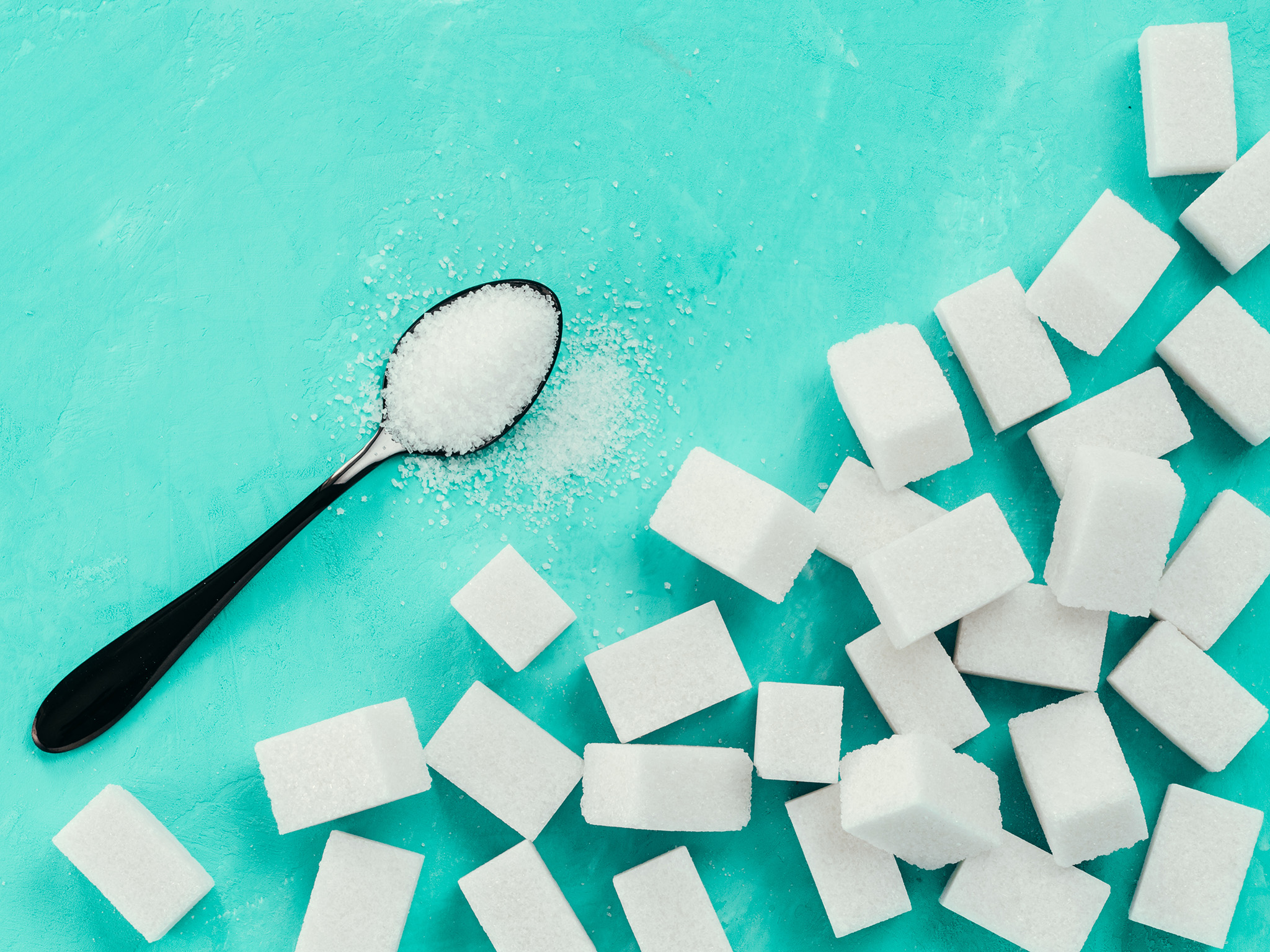 sugar on a black teaspoon with sugar cubes piled nearby